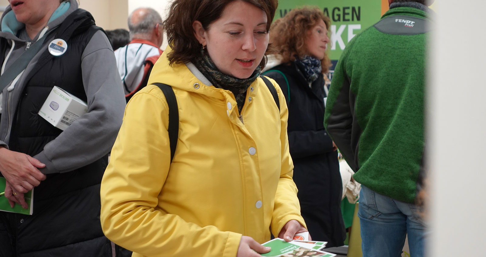 Eine Frau hört zu am Messestand. Sie hat Infomaterial in der Hand