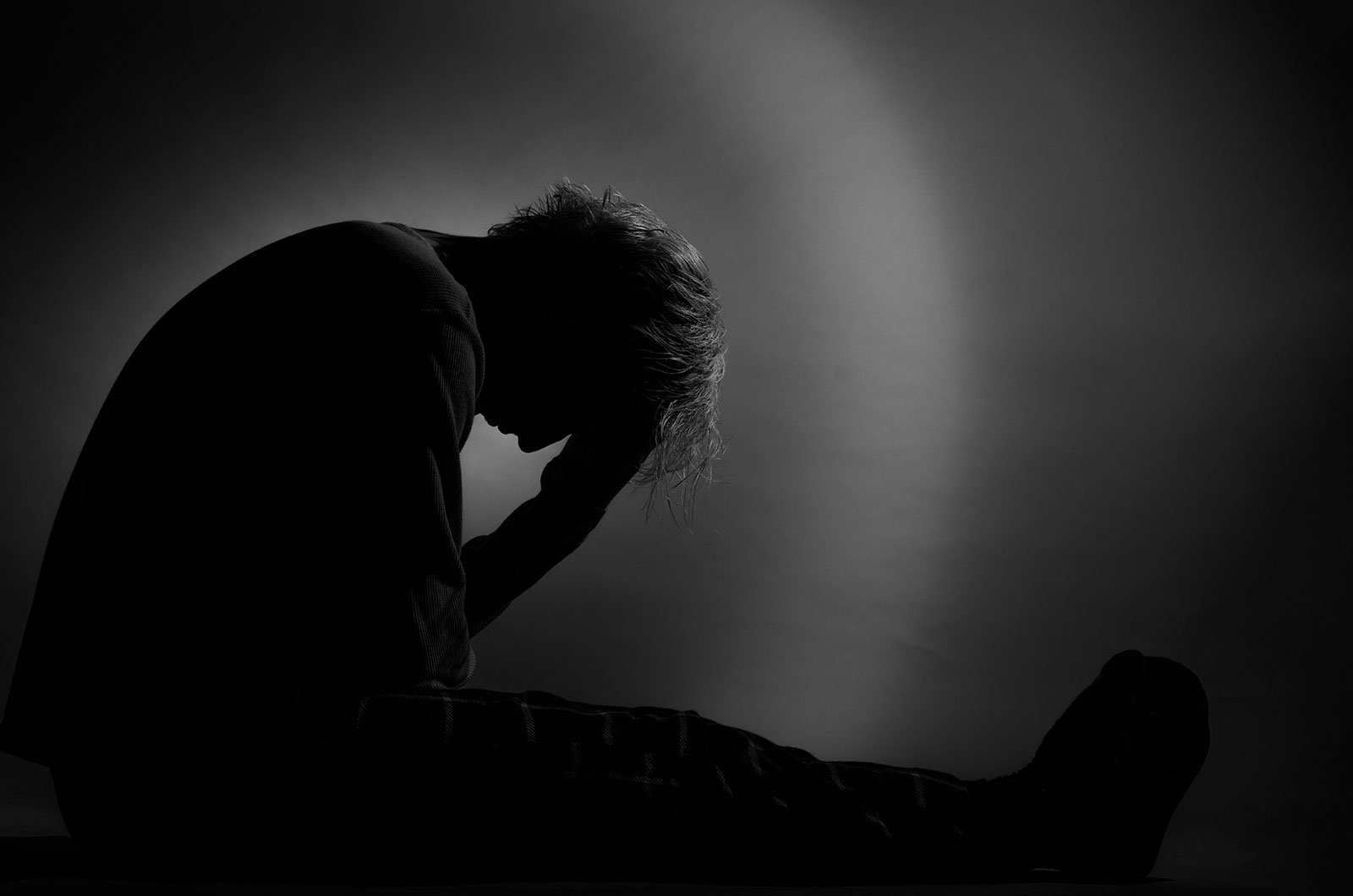 Silhouette eines einsamen Jungen, der seinen Kopf nach vorn neigt und mit beiden Händen hält