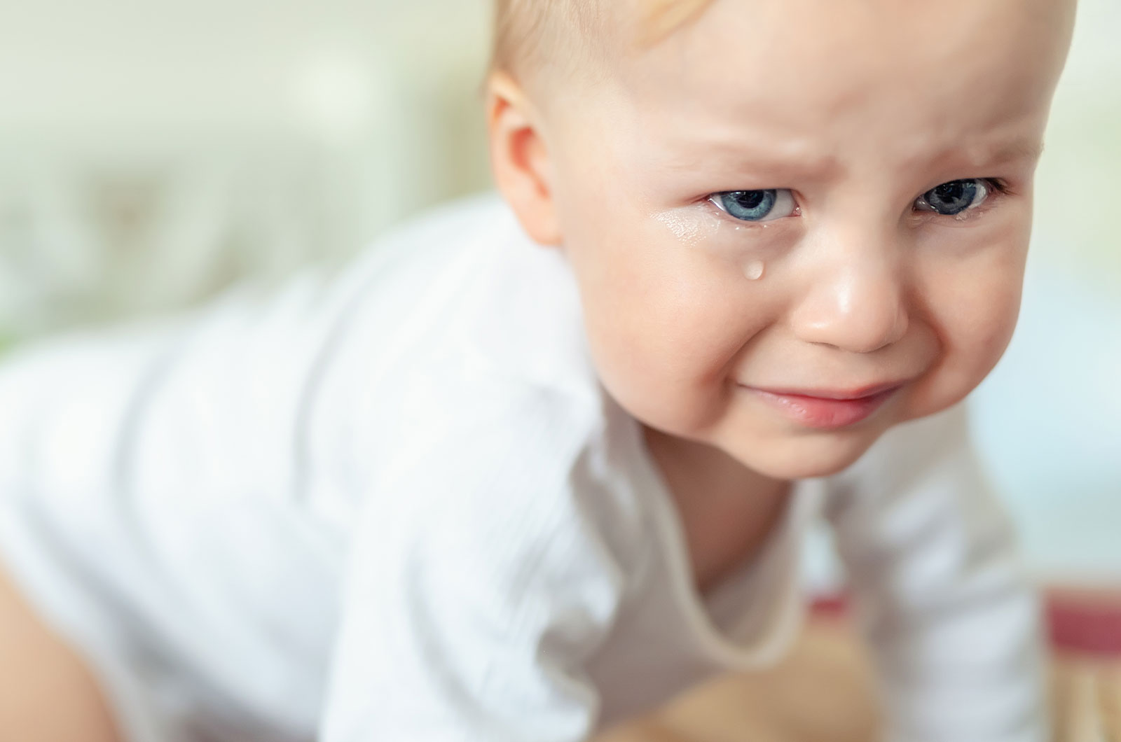 Porträt eines blonden, Jungen mit blauen Augen, im Krabbelalter, dem ein dickes Tränchen über die Wange läuft