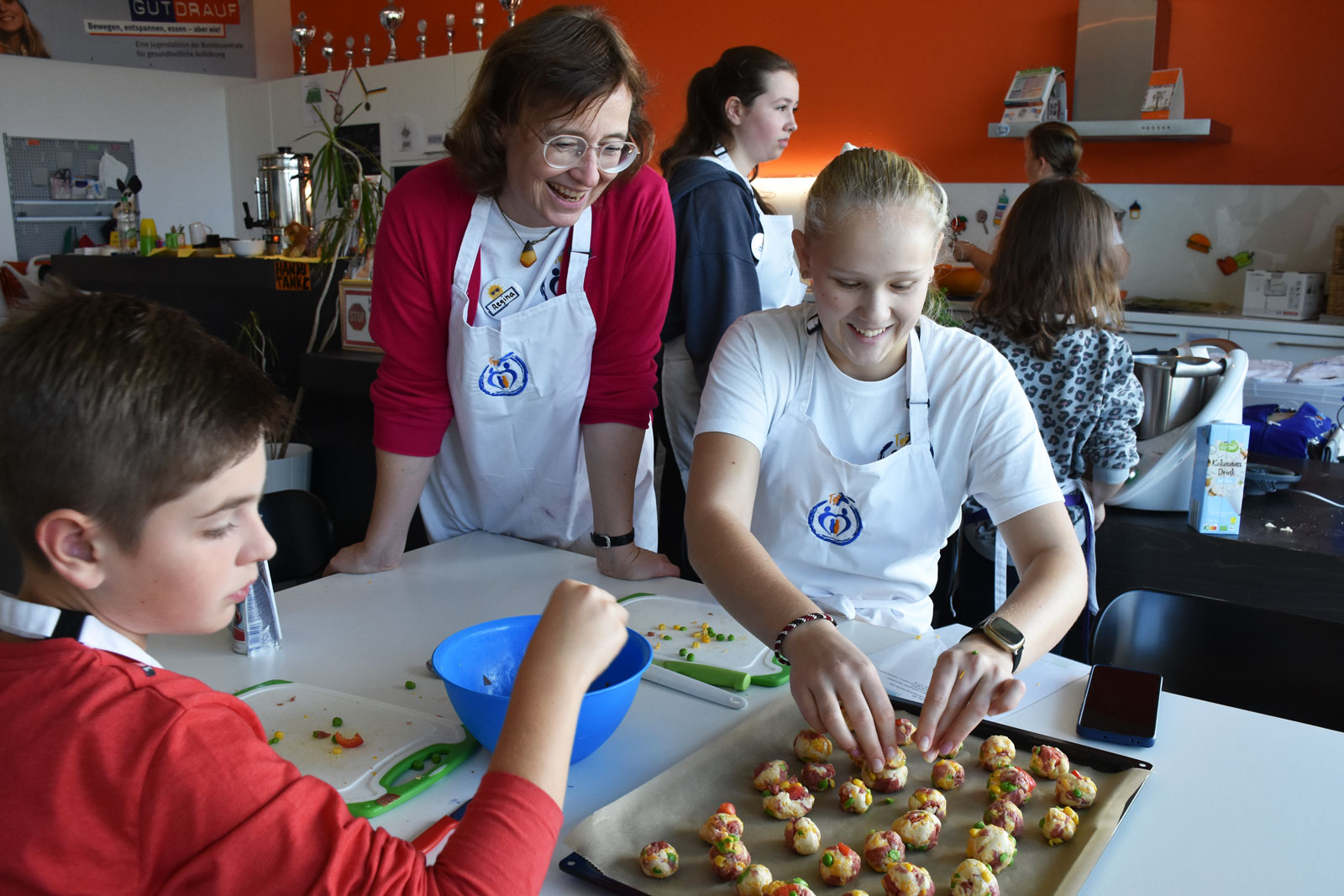 Beim Zubereiten von Pizzabällchen lachen eine erwachsene Frau und zwei Kinder