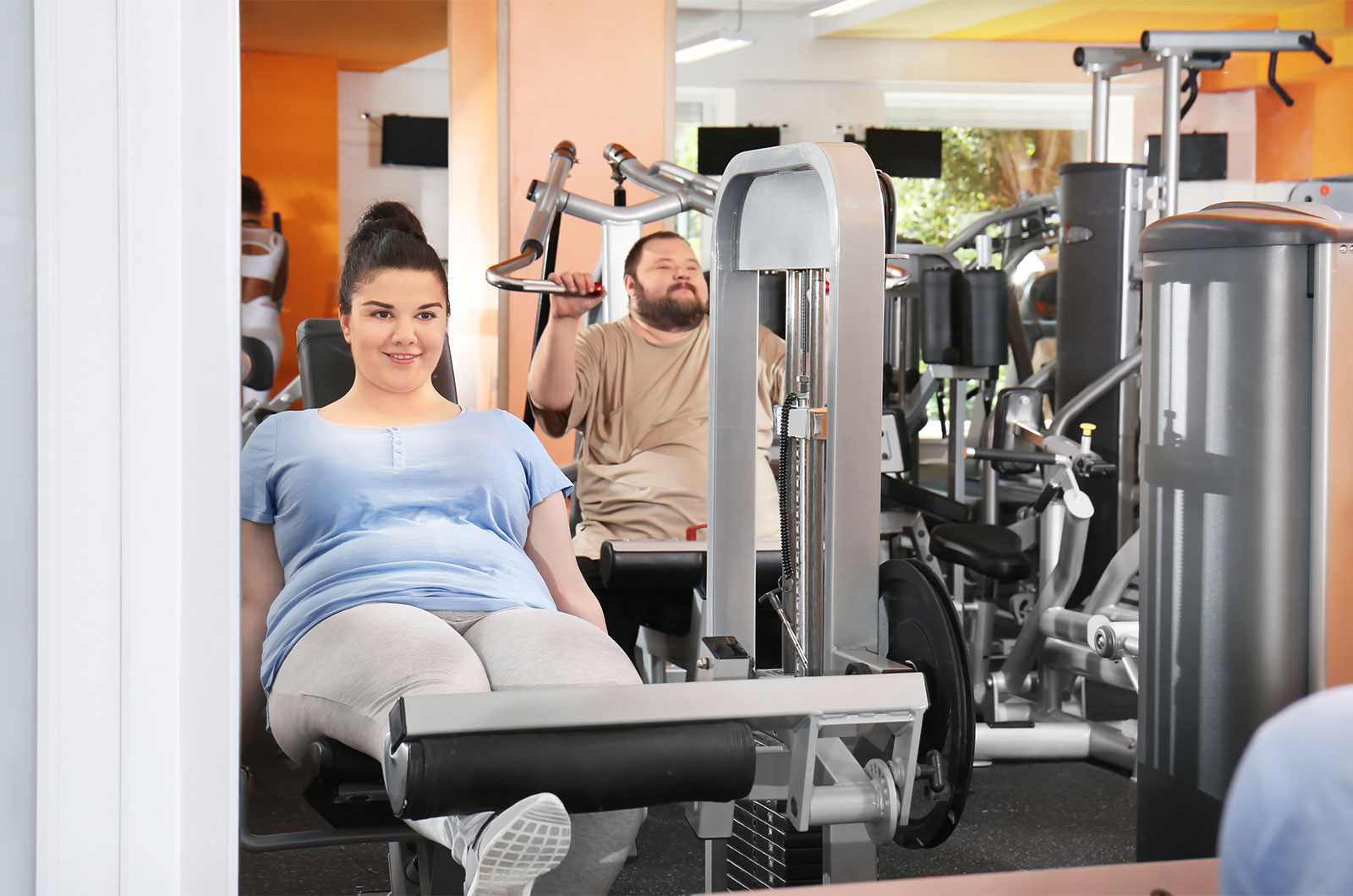 junge Frau und junger Mann, beide übergewichtig, beim Training im Fitnessstudio