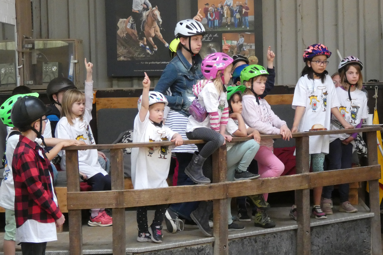 Eine große Gruppe Kinder steht in einem Reitstall und meldet sich.