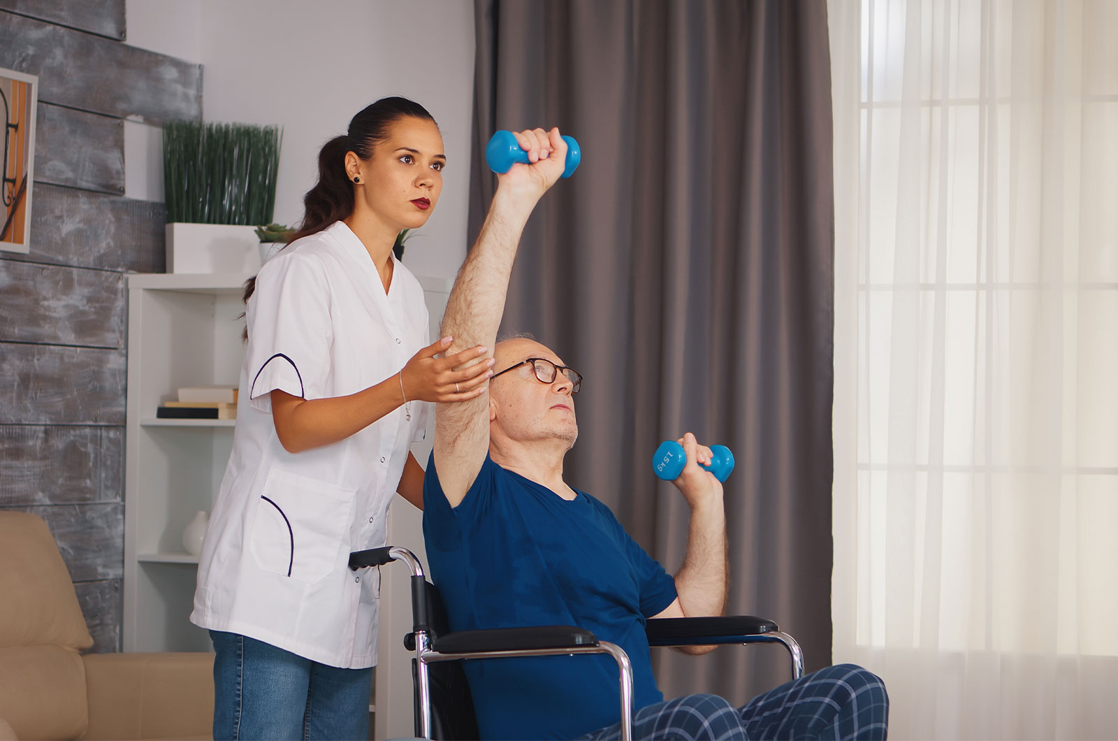 Senior im Rollstuhl erhält Unterstützung von Physiotherapeutin, Training zum Muskelaufbau