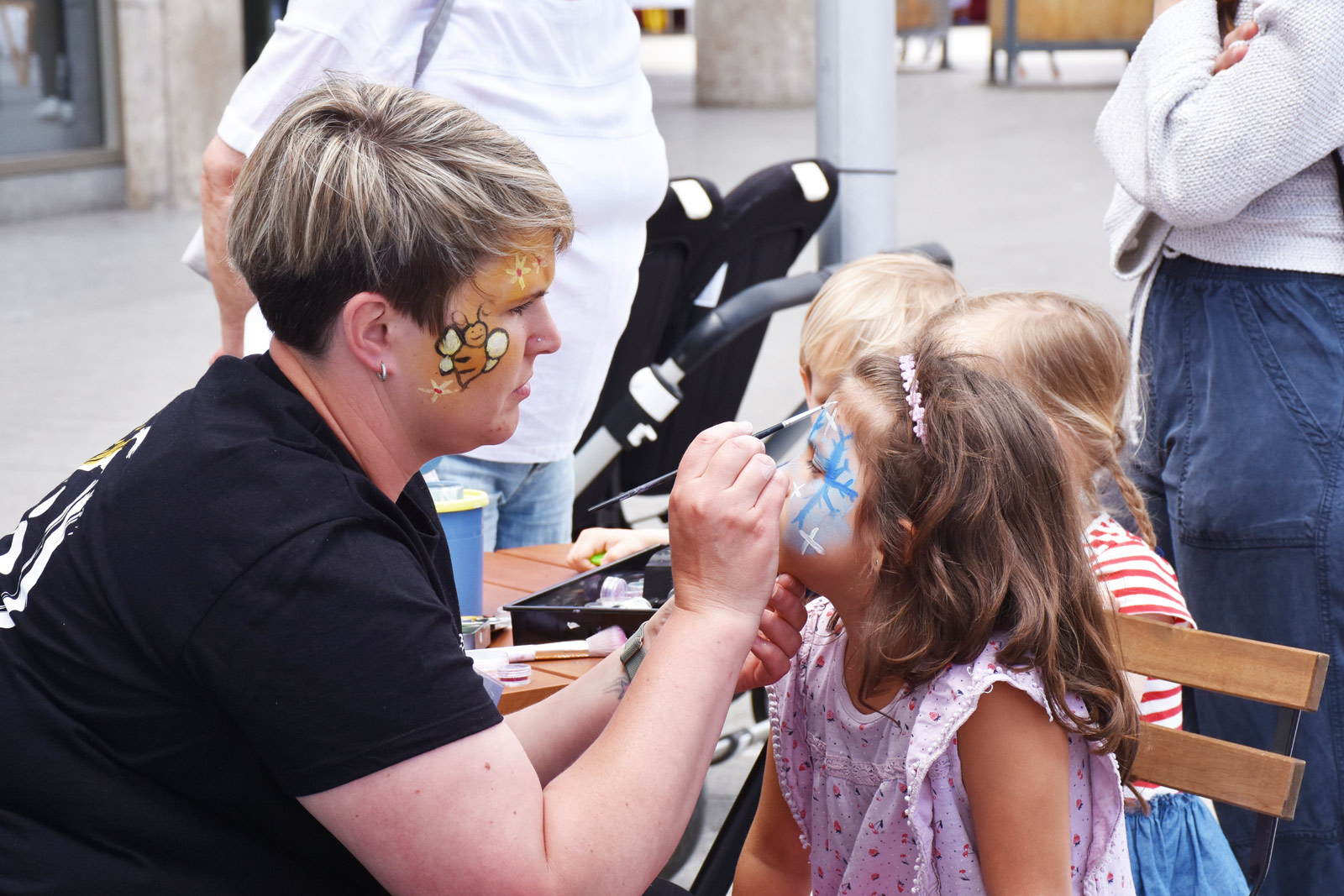 Typ-F-Kinderschminken EIn Kind wird im Gesicht mit einem bunten Motiv geschminkt.