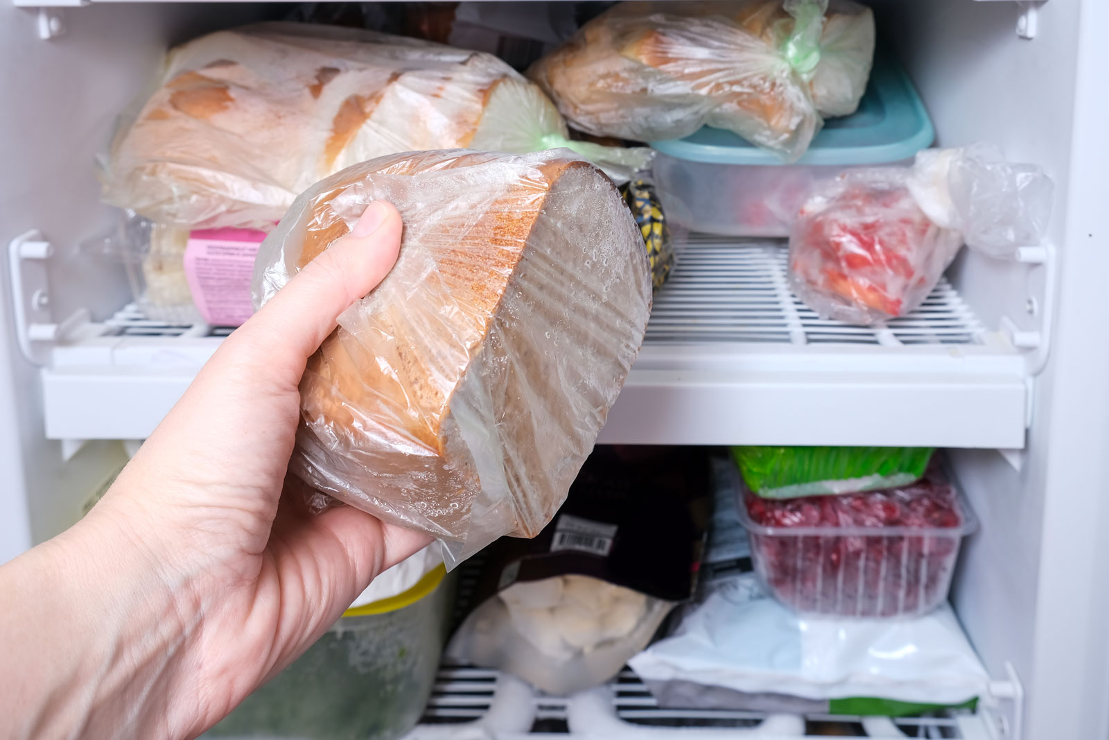 Eine Hand legt einen Laib Brot in die Tiefkühltruhe