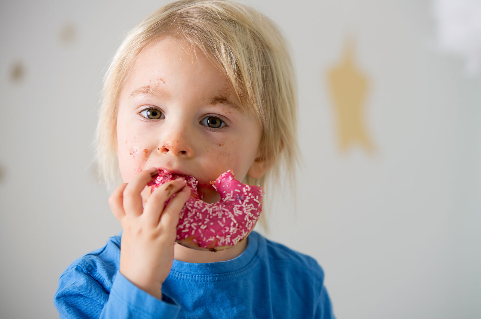 Kleinkind isst einen Donut mit bunten Zuckerstreuseln