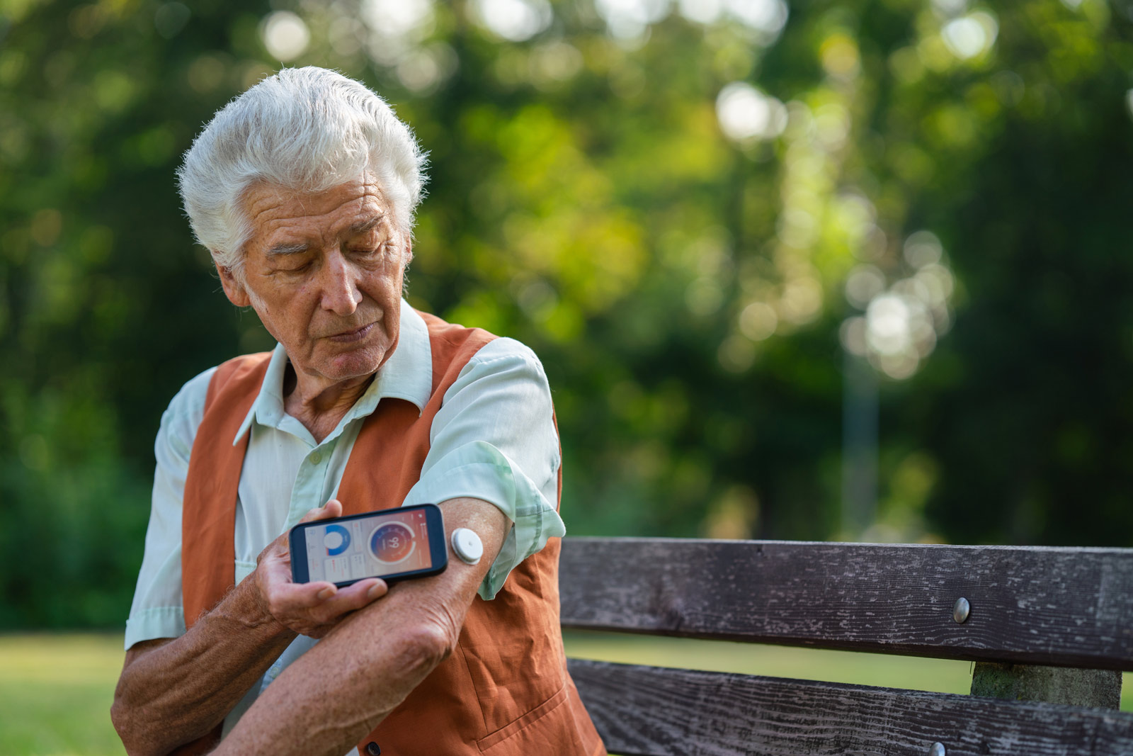 Ein älterer Mann misst sein CGM auf einer Parkbank mit dem Smartphone aus