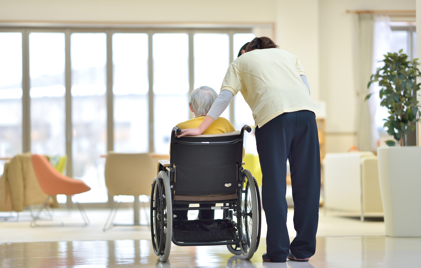 Pflege im Alter Eine alte Frau im Rollstuhl, daneben eine Pflegerin